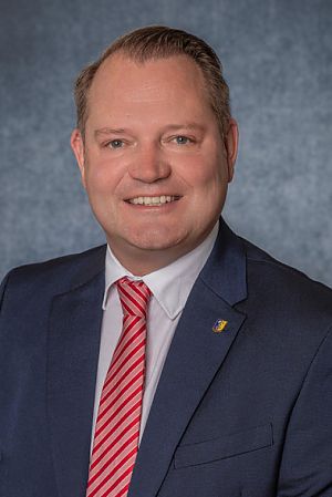 Portrait of a middle-aged smiling man, wearing a white shirt, blue jacket and red and white patterned tie